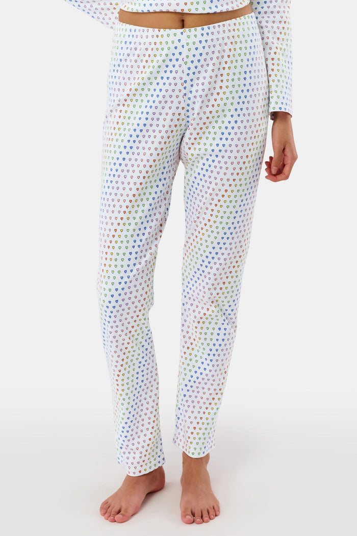 A woman stands barefoot in Roller Rabbit’s Disco Hearts Pajamas, featuring a long-sleeved, buttoned top and straight-leg pants with colorful polka dots on white for comfort and style.