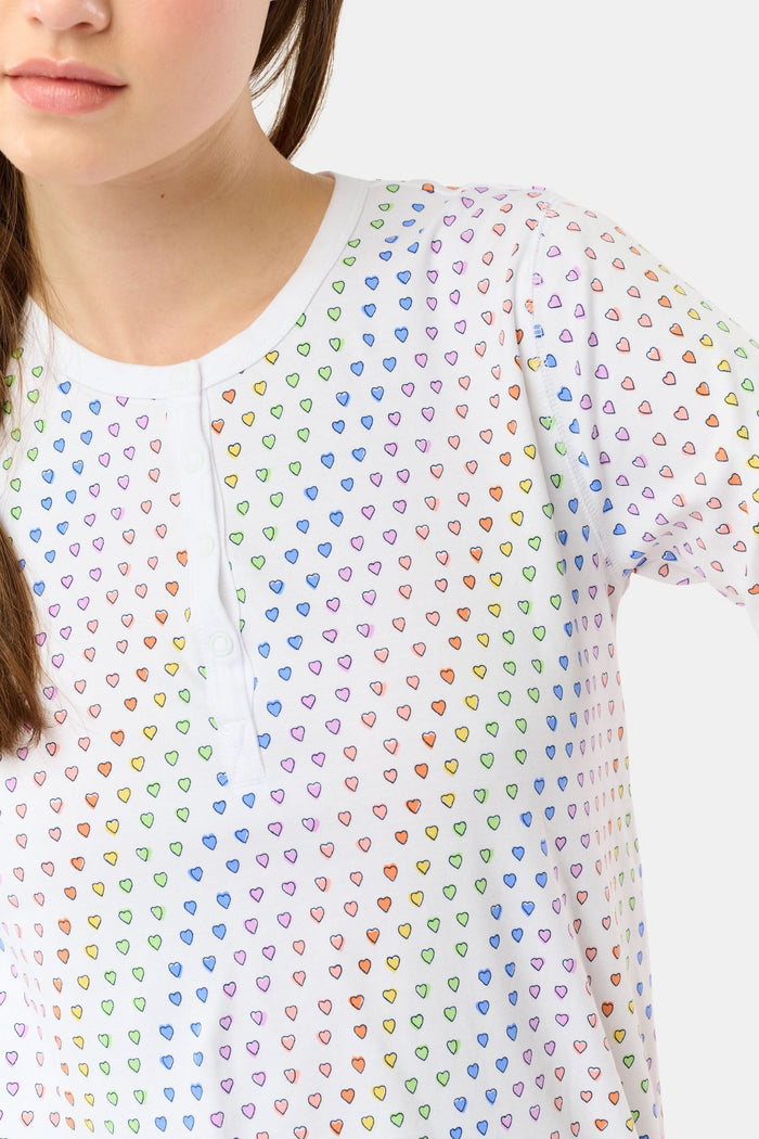 A woman stands barefoot in Roller Rabbit’s Disco Hearts Pajamas, featuring a long-sleeved, buttoned top and straight-leg pants with colorful polka dots on white for comfort and style.