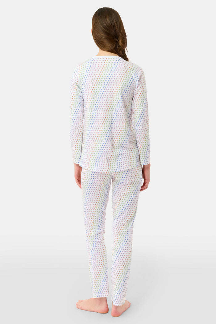 A woman stands barefoot in Roller Rabbit’s Disco Hearts Pajamas, featuring a long-sleeved, buttoned top and straight-leg pants with colorful polka dots on white for comfort and style.