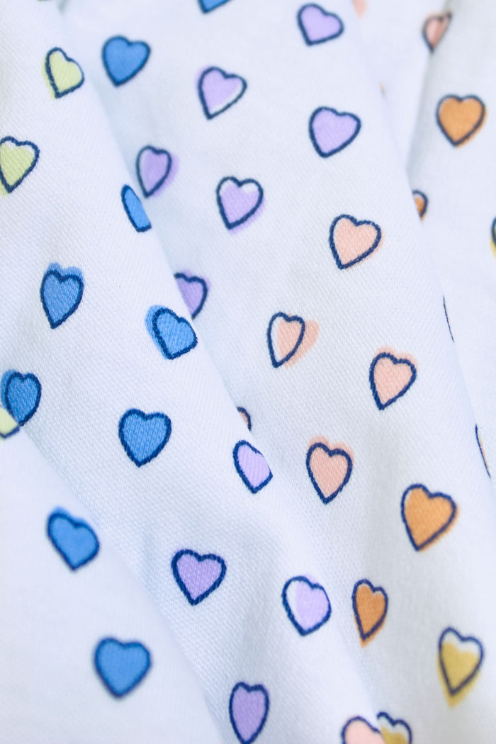 A woman stands barefoot in Roller Rabbit’s Disco Hearts Pajamas, featuring a long-sleeved, buttoned top and straight-leg pants with colorful polka dots on white for comfort and style.