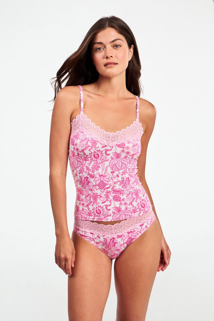 A woman with long brown hair poses confidently against a plain light background, wearing the Roller Rabbit Ditsy Amanda Perry Cami—a matching camisole and underwear set with pink and white floral lace and delicate scalloped trim.