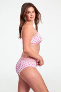 A woman poses sideways in a matching light pink Roller Rabbit Ditsy Daisy Pointelle Cornelia Hipster bra and high-waisted panties with small floral patterns and lace trim, against a plain white background.