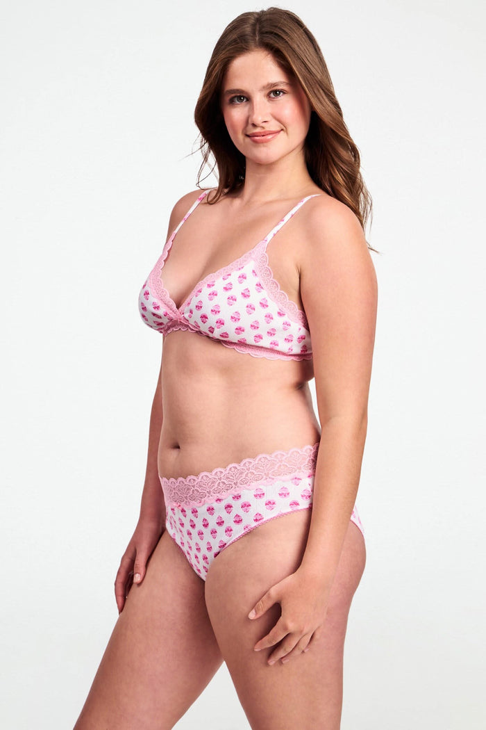 A woman wears a Roller Rabbit Ditsy Daisy Pointelle Jane Bralette—a light pink floral print bra with lace trim—standing against a plain background.