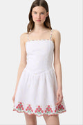 A woman wearing the Roller Rabbit Ditsy Floral Embroidery Hannah Dress—white linen with thin straps, red floral embroidery at the hem and neckline, and yellow flower details—stands against a plain light background.