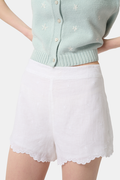 A person wears the Roller Rabbit Ditsy Floral Embroidery Jordana Shorts—white, high-waisted, with a subtle floral design and scalloped lace trim—paired with a light green buttoned sleeveless knit top. The background is plain white.