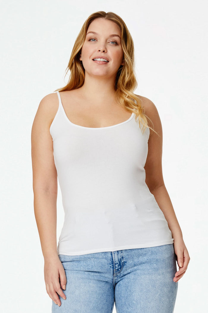 A woman with long, wavy blonde hair models the Roller Rabbit Dream Camisole in white with light blue jeans, standing against a plain white background and smiling gently at the camera.