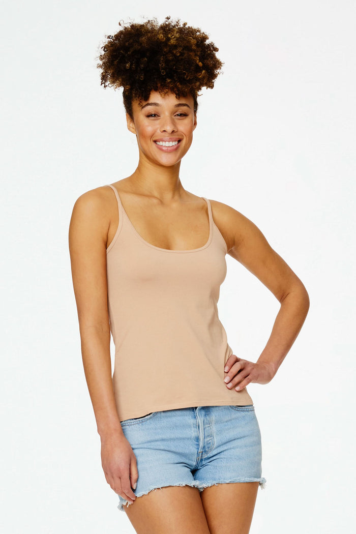 A smiling woman with curly hair wears the Roller Rabbit Dream Camisole in beige and light blue denim shorts, posing with one hand on her hip against a plain white background.