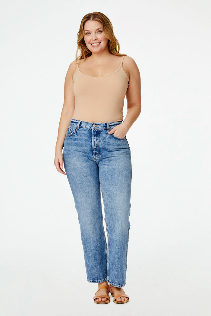 A smiling woman with curly hair wears the Roller Rabbit Dream Camisole in beige and light blue denim shorts, posing with one hand on her hip against a plain white background.