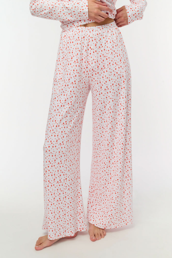 A person wears Roller Rabbit's Étoiles Boden Pant—loose white Pima cotton pajama pants with a red Étoiles print—paired with a matching top. Only their lower body is visible as they stand barefoot against a plain white background.