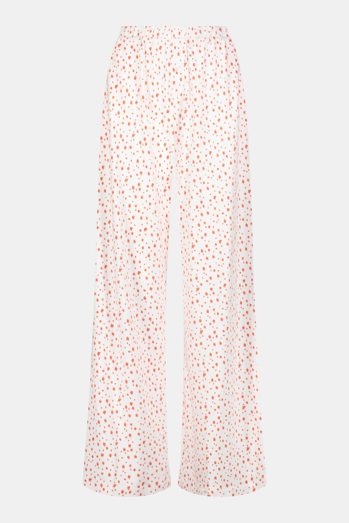 A person wears Roller Rabbit's Étoiles Boden Pant—loose white Pima cotton pajama pants with a red Étoiles print—paired with a matching top. Only their lower body is visible as they stand barefoot against a plain white background.