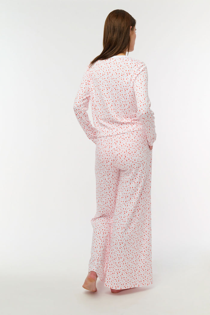 A person wears Roller Rabbit's Étoiles Boden Pant—loose white Pima cotton pajama pants with a red Étoiles print—paired with a matching top. Only their lower body is visible as they stand barefoot against a plain white background.
