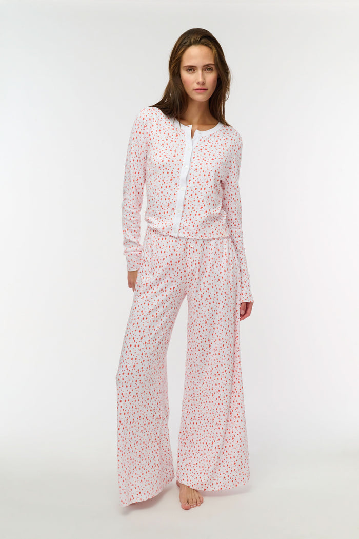 A person wears Roller Rabbit's Étoiles Boden Pant—loose white Pima cotton pajama pants with a red Étoiles print—paired with a matching top. Only their lower body is visible as they stand barefoot against a plain white background.