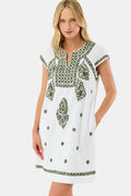 A woman in the Roller Rabbit Faith Dress—a 100 cotton midi with green floral and geometric embroidery—stands with one hand in her pocket against a plain light background.