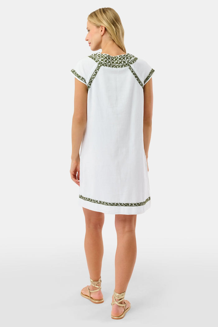 A woman in the Roller Rabbit Faith Dress—a 100 cotton midi with green floral and geometric embroidery—stands with one hand in her pocket against a plain light background.