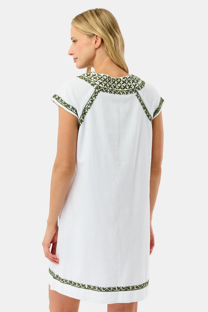 A woman in the Roller Rabbit Faith Dress—a 100 cotton midi with green floral and geometric embroidery—stands with one hand in her pocket against a plain light background.