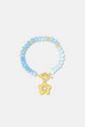 The Roller Rabbit Flower Charm Beaded Bracelet features light blue round beads with gold spacers, a gold flower-shaped charm, and a gold toggle clasp, displayed on a plain white background.