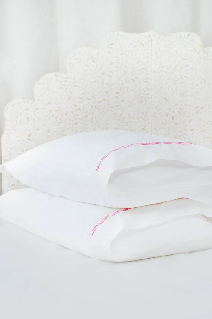 Two white Francis Embroidered Pillowcases by Roller Rabbit, made of 100 cotton with a 300 thread count, are arranged on a matching bed. A scalloped, floral headboard provides an elegant backdrop.