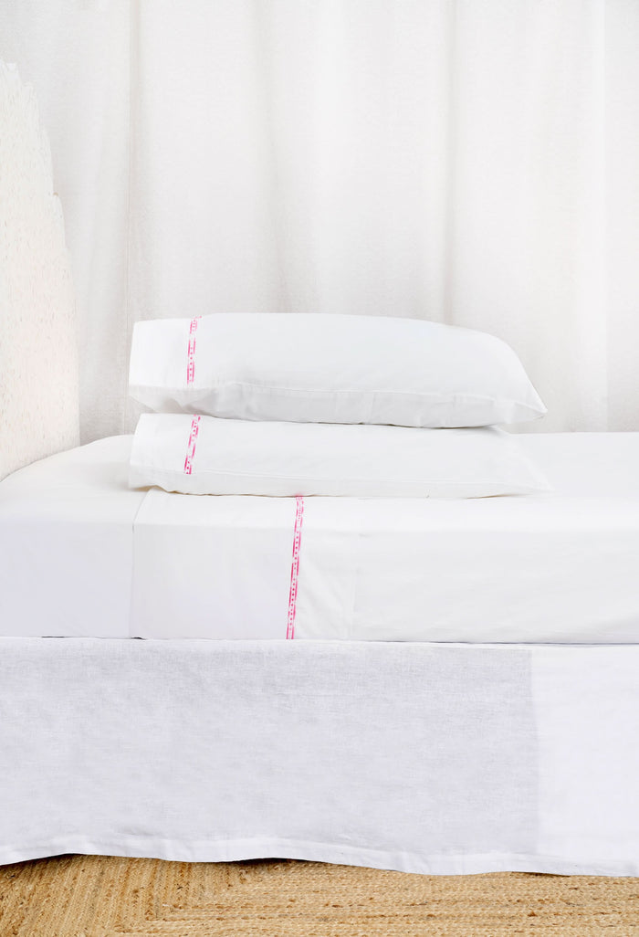 Two white Francis Embroidered Pillowcases by Roller Rabbit, made of 100 cotton with a 300 thread count, are arranged on a matching bed. A scalloped, floral headboard provides an elegant backdrop.