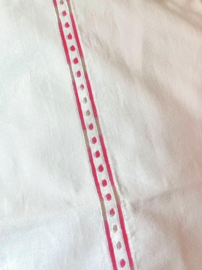 Two white Francis Embroidered Pillowcases by Roller Rabbit, made of 100 cotton with a 300 thread count, are arranged on a matching bed. A scalloped, floral headboard provides an elegant backdrop.