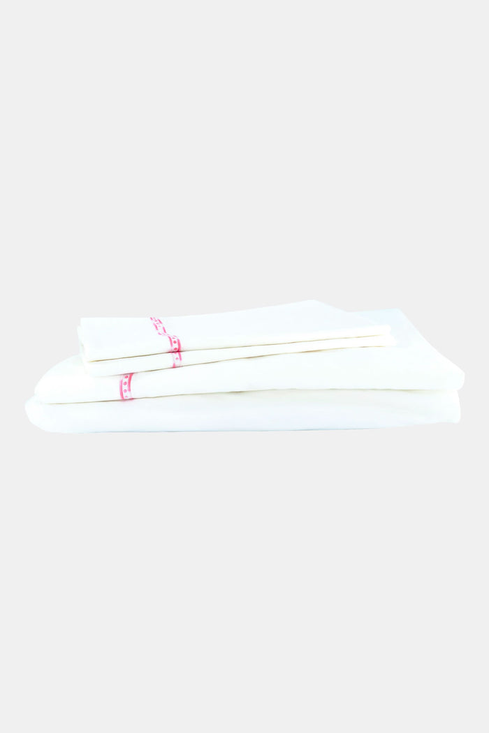 The Francis Embroidered Sheet Set by Roller Rabbit features white cotton sheets and pillowcases with a thin pink border, perfectly complementing an ornate white patterned headboard for a clean, elegant look.