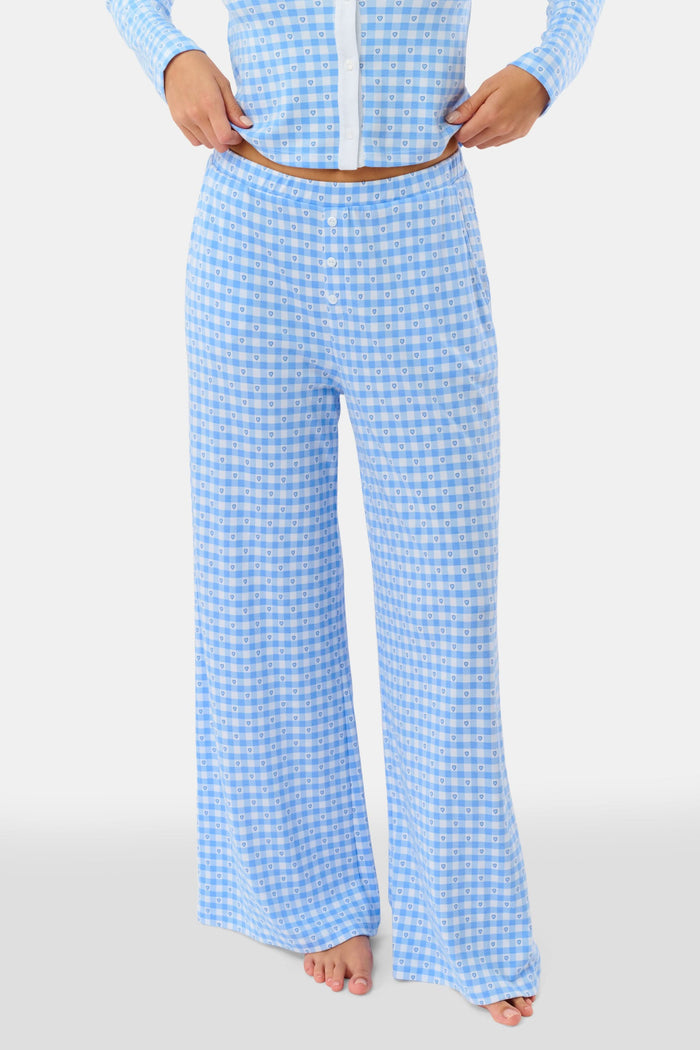 A person stands barefoot wearing Roller Rabbit’s Gingham Hearts Boden Pant—light blue, wide-leg Pima cotton pants with an elastic waist—and a matching long-sleeve top with blue gingham hearts. Their hands rest on their hips. Head and feet are out of frame.