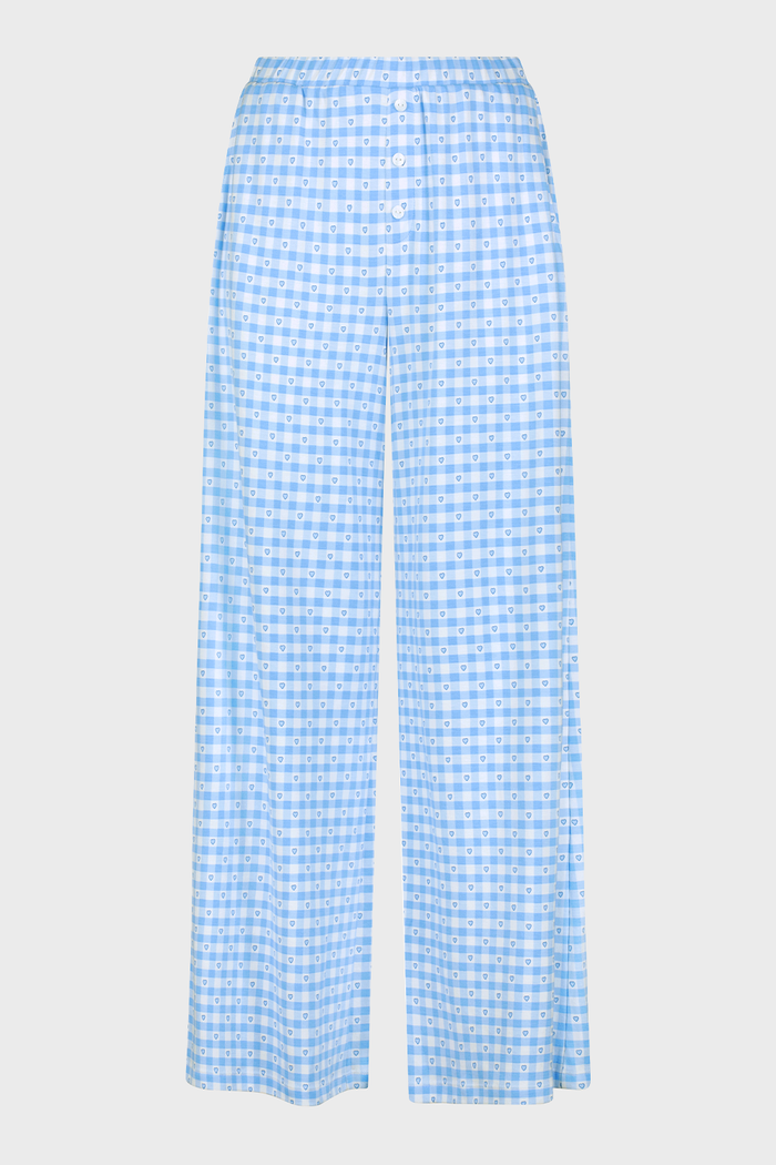 A person stands barefoot wearing Roller Rabbit’s Gingham Hearts Boden Pant—light blue, wide-leg Pima cotton pants with an elastic waist—and a matching long-sleeve top with blue gingham hearts. Their hands rest on their hips. Head and feet are out of frame.