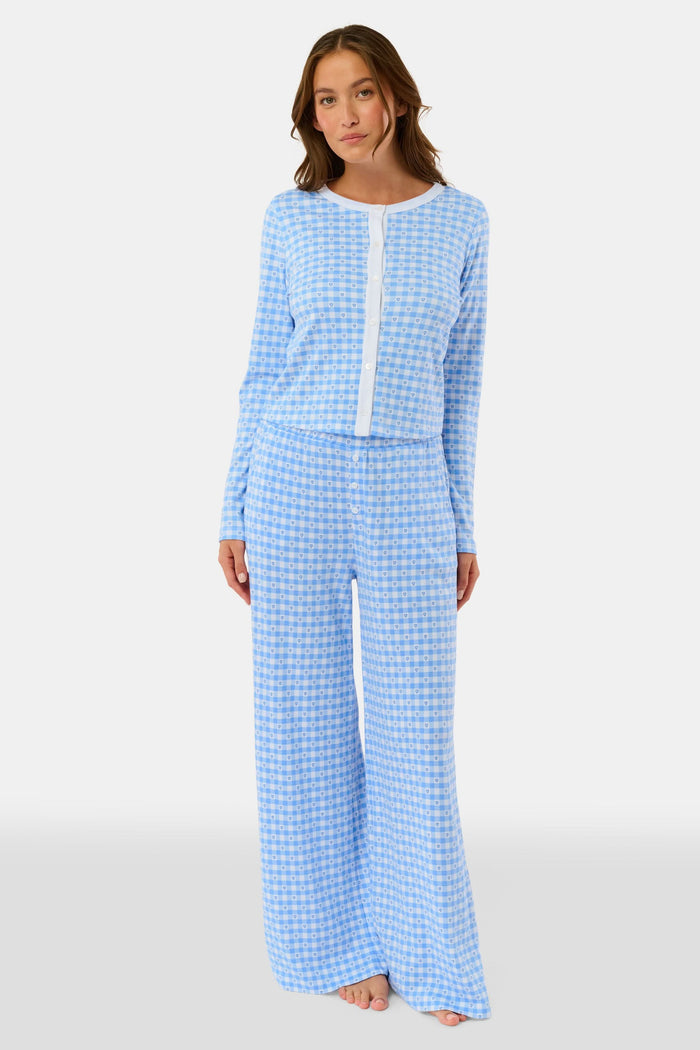 A person stands barefoot wearing Roller Rabbit’s Gingham Hearts Boden Pant—light blue, wide-leg Pima cotton pants with an elastic waist—and a matching long-sleeve top with blue gingham hearts. Their hands rest on their hips. Head and feet are out of frame.