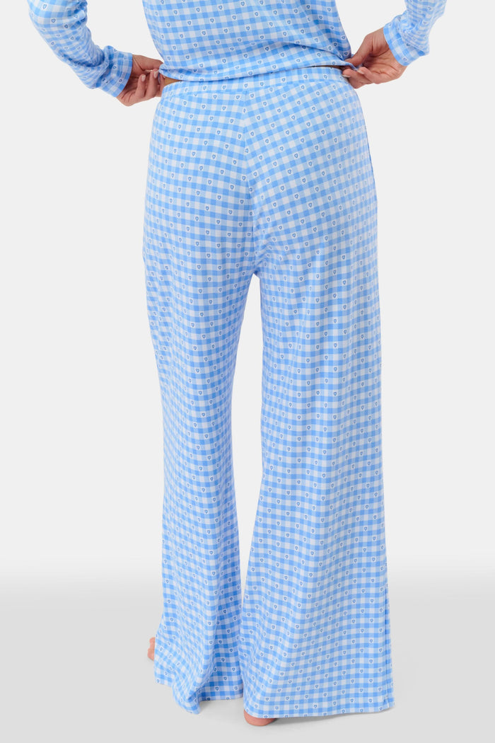 A person stands barefoot wearing Roller Rabbit’s Gingham Hearts Boden Pant—light blue, wide-leg Pima cotton pants with an elastic waist—and a matching long-sleeve top with blue gingham hearts. Their hands rest on their hips. Head and feet are out of frame.