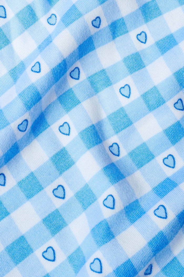 A woman in the Roller Rabbit Gingham Hearts Nessa Cardigan, featuring a blue gingham hearts pattern and button-up front, stands against a plain background, adding a charming touch to her cozy look.