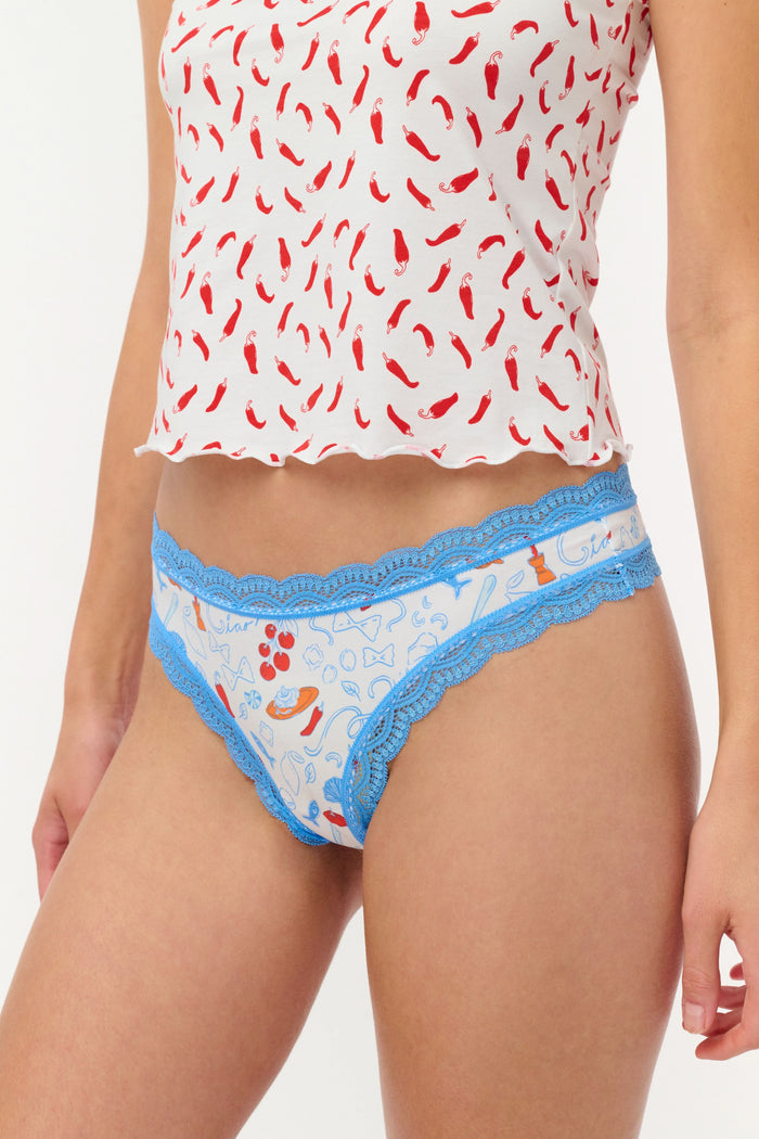 The Roller Rabbit Globe Trotter Thong 4 Pack features four women's lace trim thongs in blue, red, pink, and light pink, each with playful patterns and prints, displayed in two rows on a light background.