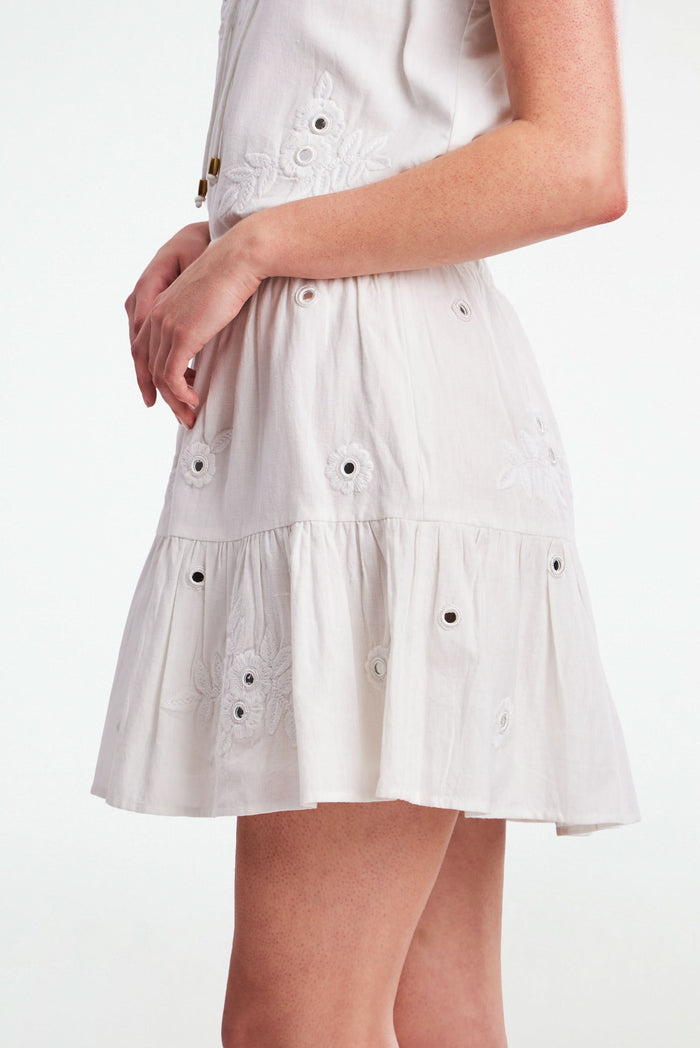 A woman models the Roller Rabbit Gloriosa Embroidery Fleet Skirt, featuring floral embroidery and eyelet details. The image captures her from waist to mid-thigh, showcasing the skirt’s delicate cotton design with one hand in her pocket.