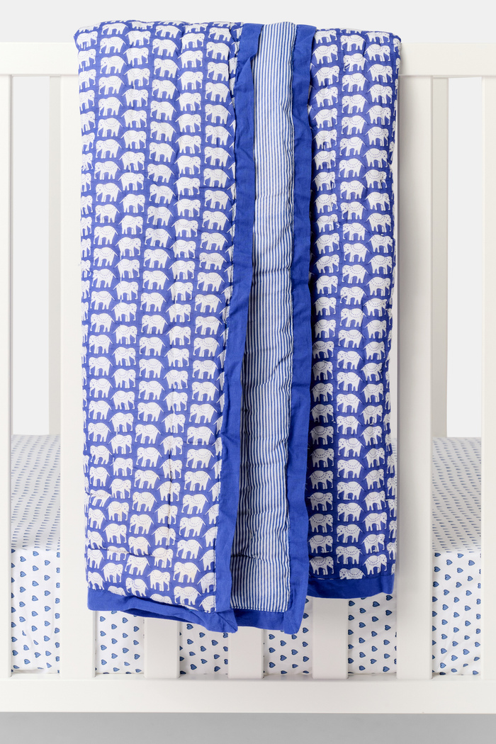 The Roller Rabbit Hathi Baby Quilt features a blue background with a white elephant print, blue and white striped lining, and a solid blue border, all crafted from soft cotton for comfort.