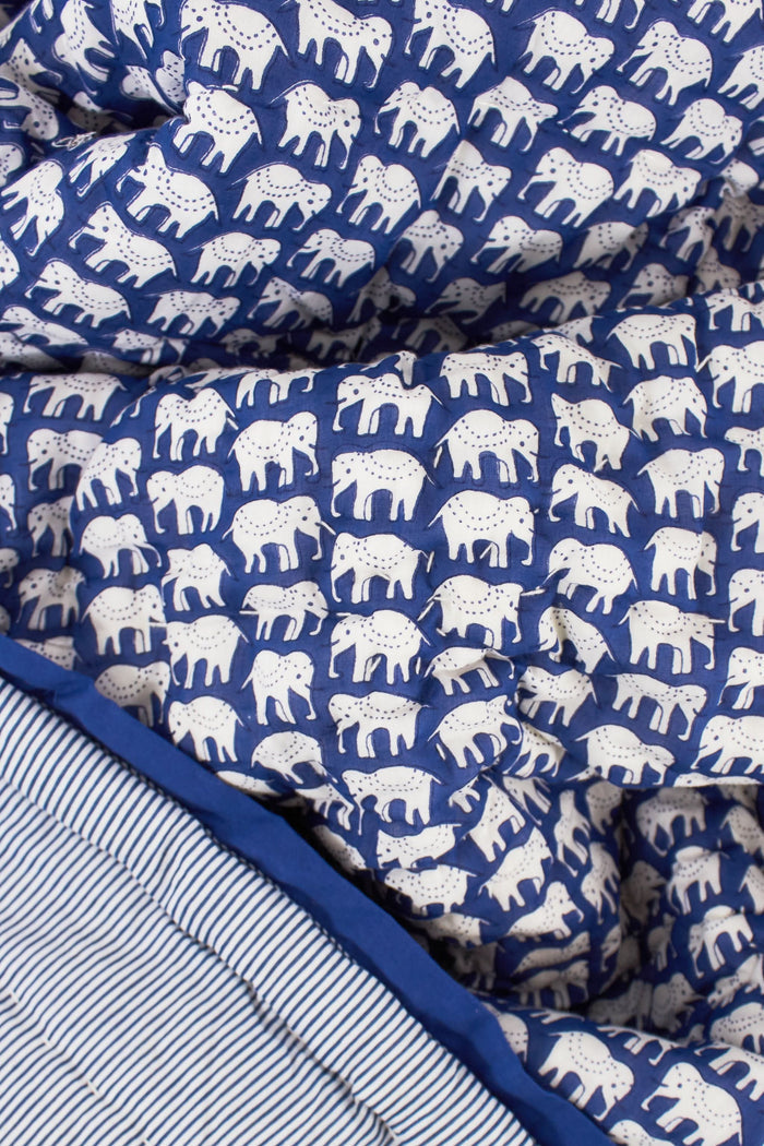 The Roller Rabbit Hathi Baby Quilt features a blue background with a white elephant print, blue and white striped lining, and a solid blue border, all crafted from soft cotton for comfort.