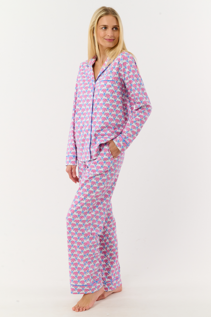 A woman stands barefoot against a white background, wearing Roller Rabbit Hathi Hearts Long Sleeve Polo Pajamas featuring a colorful pink, blue, and white floral pattern.