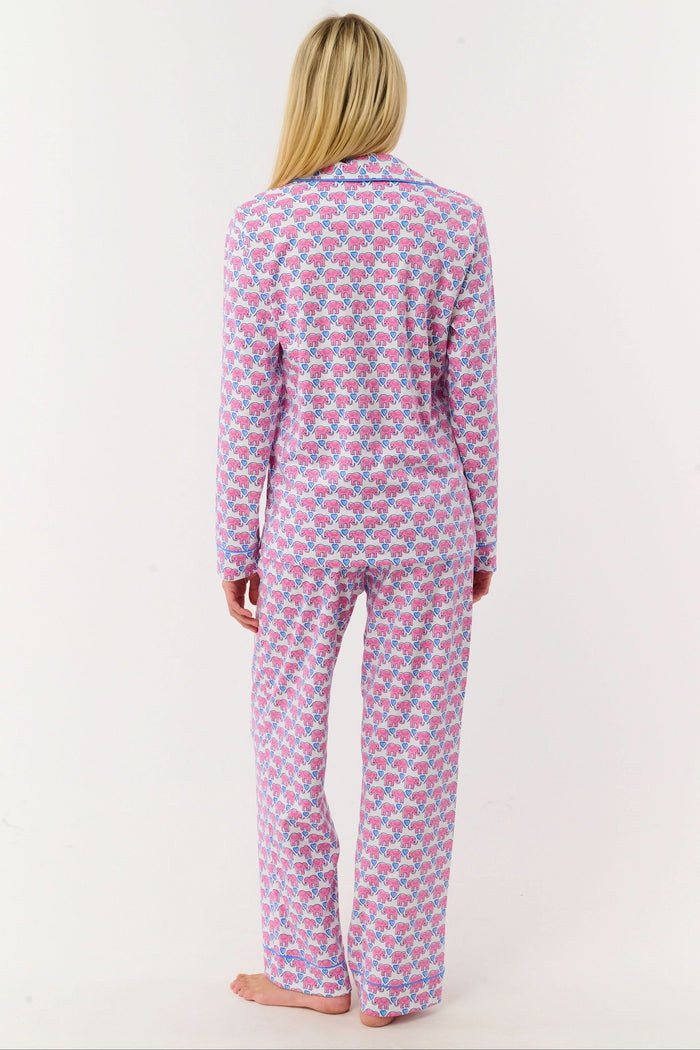 A woman stands barefoot against a white background, wearing Roller Rabbit Hathi Hearts Long Sleeve Polo Pajamas featuring a colorful pink, blue, and white floral pattern.