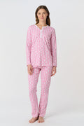 A woman stands barefoot in Roller Rabbit Hathi Pajamas—pink and white with long sleeves and pants—smiling softly against a plain white background.