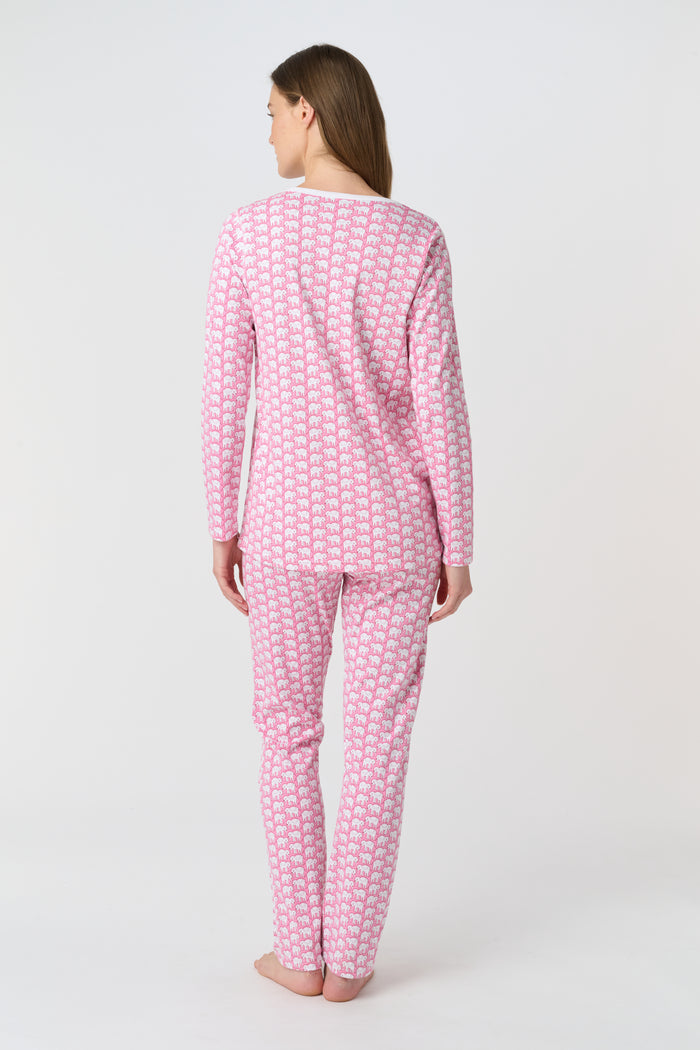A woman stands barefoot in Roller Rabbit Hathi Pajamas—pink and white with long sleeves and pants—smiling softly against a plain white background.