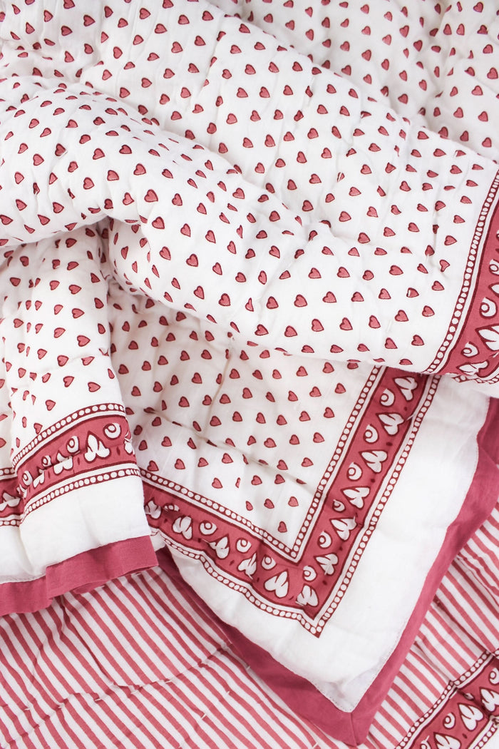 The Roller Rabbit Hearts Baby Quilt features a white cotton background with small red hearts print and a red and white border adorned with geometric and floral designs.