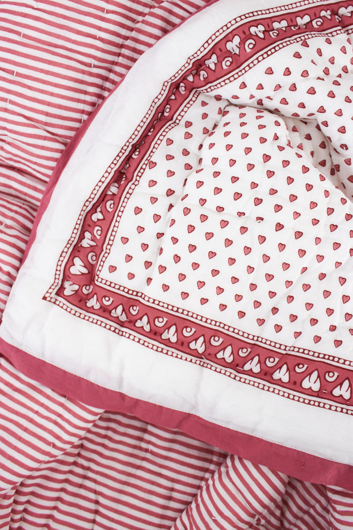 The Roller Rabbit Hearts Baby Quilt features a white cotton background with small red hearts print and a red and white border adorned with geometric and floral designs.