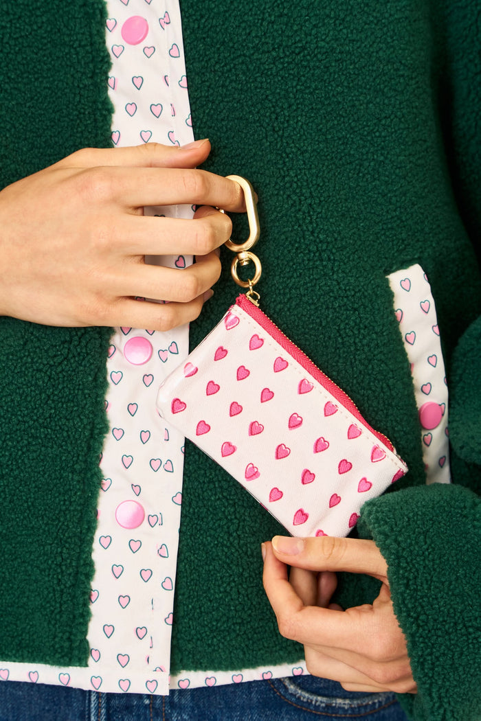 The Roller Rabbit Hearts Coin Pouch is a small white cotton canvas pouch with pink watercolor hearts, a red zipper, and a gold keyring and clasp, shown against a plain white background.