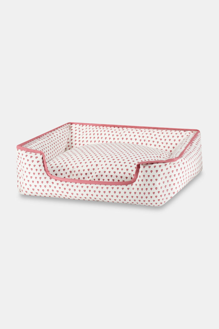 The Roller Rabbit Hearts Dog Bed is a rectangular, washable bed with a low front opening, white fabric adorned with red hearts, and red piping. It combines comfort and style for your pet.