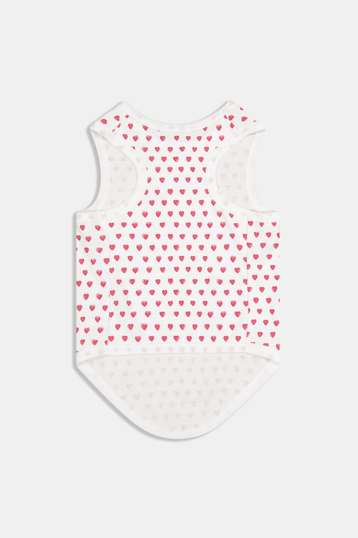 A brown poodle sits on a white background wearing Roller Rabbit's Hearts Dog Pajamas, adorable Pima Cotton pet PJs featuring small pink heart patterns for perfect matching dog pajamas.