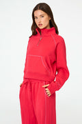 A woman with long brown hair and a neutral expression wears the cherry red Roller Rabbit Hearts Embroidered Hudson Sweatshirt, a cotton fleece half-zip pullover with a front pocket and small heart outlines on the sleeve.