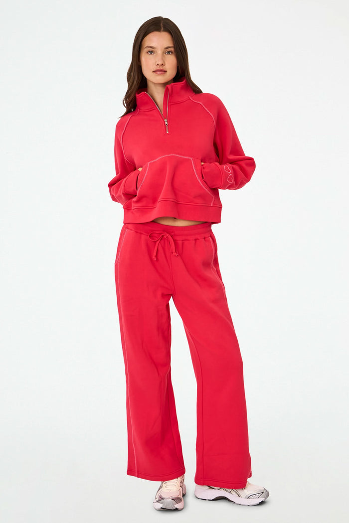 A woman with long brown hair and a neutral expression wears the cherry red Roller Rabbit Hearts Embroidered Hudson Sweatshirt, a cotton fleece half-zip pullover with a front pocket and small heart outlines on the sleeve.
