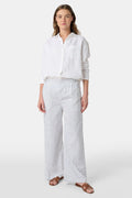 A person stands facing forward, wearing Roller Rabbit’s Hearts Kaylee Pant and a white cotton button-up shirt with brown flat sandals against a plain light background.