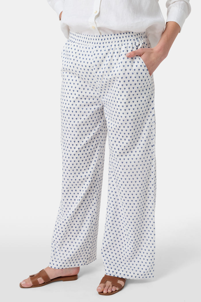 A person stands facing forward, wearing Roller Rabbit’s Hearts Kaylee Pant and a white cotton button-up shirt with brown flat sandals against a plain light background.