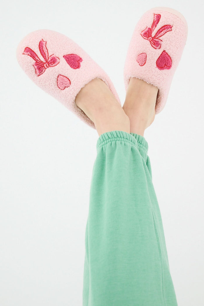 The Roller Rabbit Hearts N' Bows Fuzzy Slipper, shown from above on a white background, features pink fuzzy material with a red and pink floral embroidery and a durable rubber sole for comfort and support.