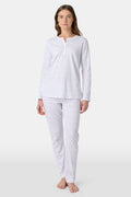 A woman stands barefoot in Roller Rabbit's Hearts Pajamas—a white, long-sleeve cotton set with a light lavender heart pattern, a round buttoned neckline top, and full-length pants—posed against a plain white background.