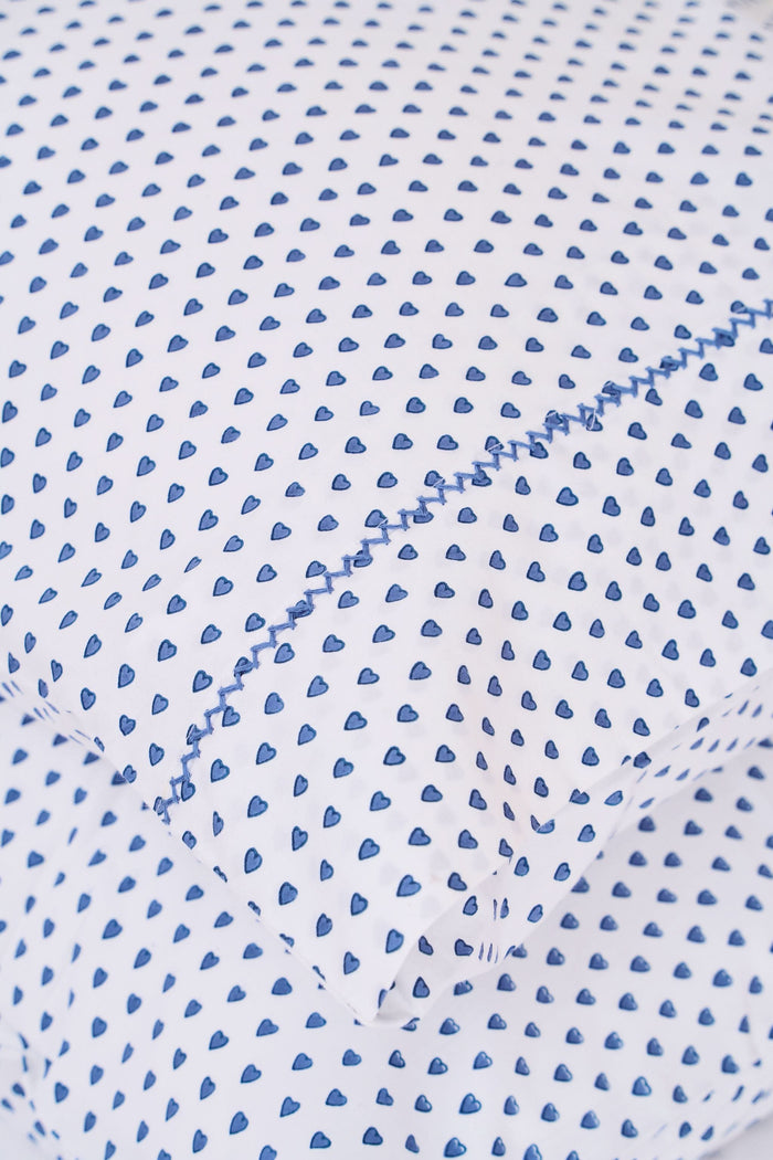 The Roller Rabbit Hearts Pillowcase Set features two white 100 cotton pillowcases with small blue leaf patterns, offering breathable comfort and style to your space. Shown stacked on a white surface against a cream-colored background.
