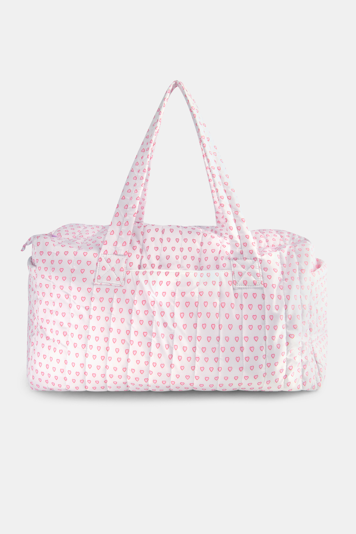 The Hearts Quilted Weekender by Roller Rabbit is a pink and white canvas bag with two handles, featuring a repeating pattern of small pink hearts on a white background.